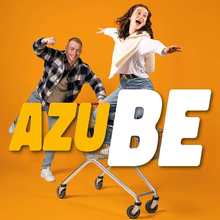 Eine Person schiebt dynamisch einen Einkaufswagen, in dem eine Person mit ausgebreiteten Armen steht. Daneben steht der Slogan: AZUBE Eine Person schiebt dynamisch einen Einkaufswagen, in dem eine Person mit ausgebreiteten Armen steht. Daneben steht der Slogan: AZUBE