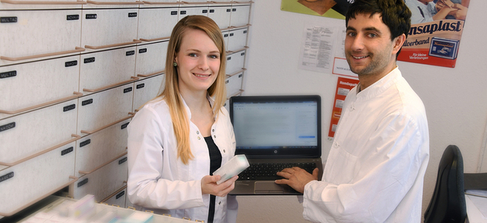 Zwei Mitarbeitende in einer Apotheke mit Laptop und vor Medikamentenregalen Zwei Mitarbeitende in einer Apotheke mit Laptop und vor Medikamentenregalen
