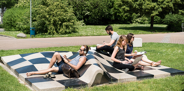 4 junge Menschen sitzen entspannt auf einer schachbrettartigen Skulpur im Park 4 junge Menschen sitzen entspannt auf einer schachbrettartigen Skulpur im Park